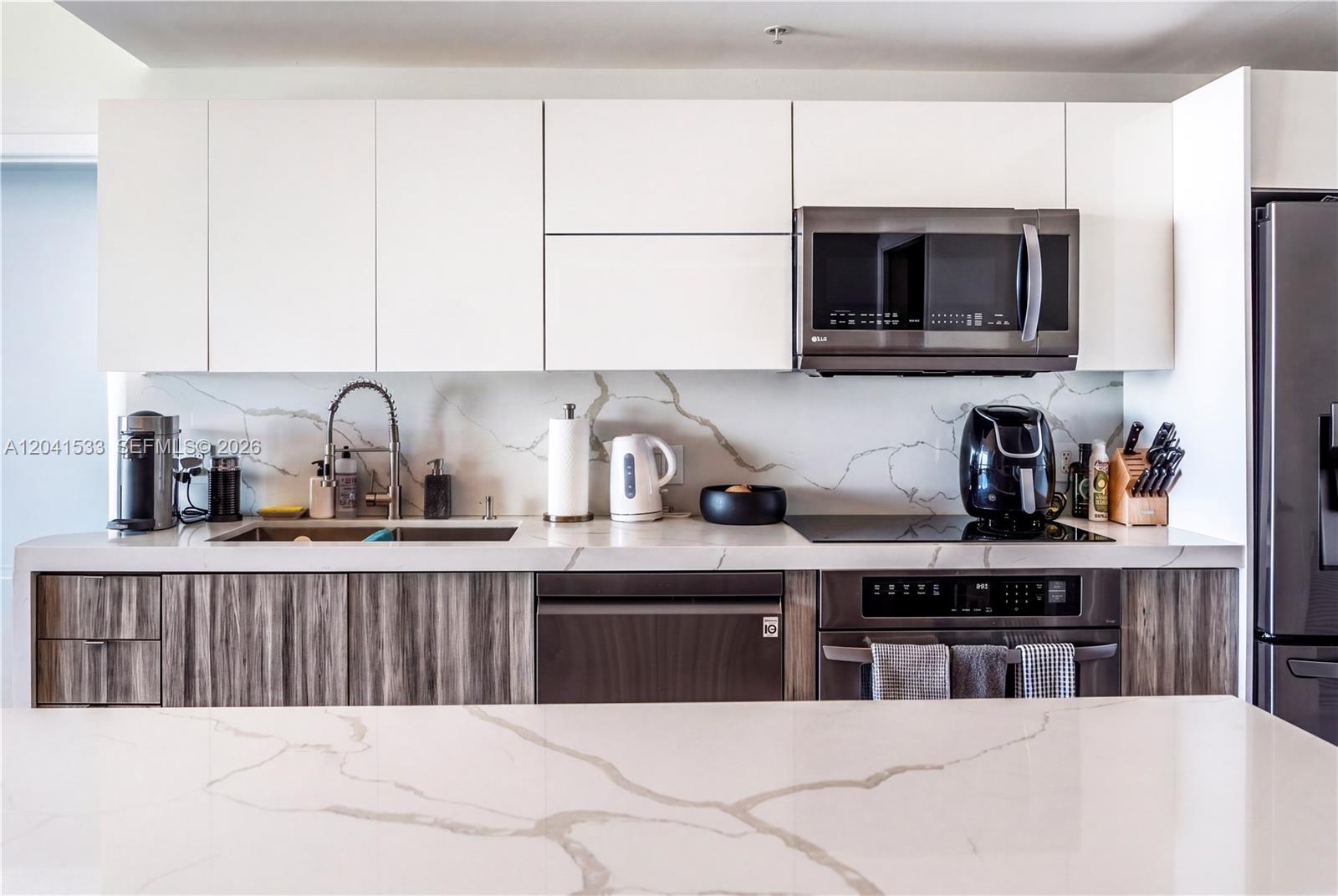 A modern kitchen features white upper cabinets, wood-grain lower cabinets, and marble-patterned countertops and backsplash — 90 SW 3rd St # 3703, Miami FL 33130, MIAMI, FL