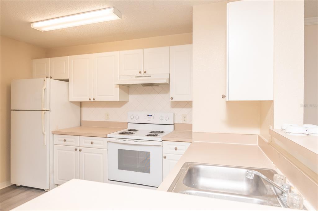 A kitchen features white cabinets, a white refrigerator, a white stove, and a stainless sink — 18001 RICHMOND PLACE DRIVE UNIT 834, TAMPA, FL