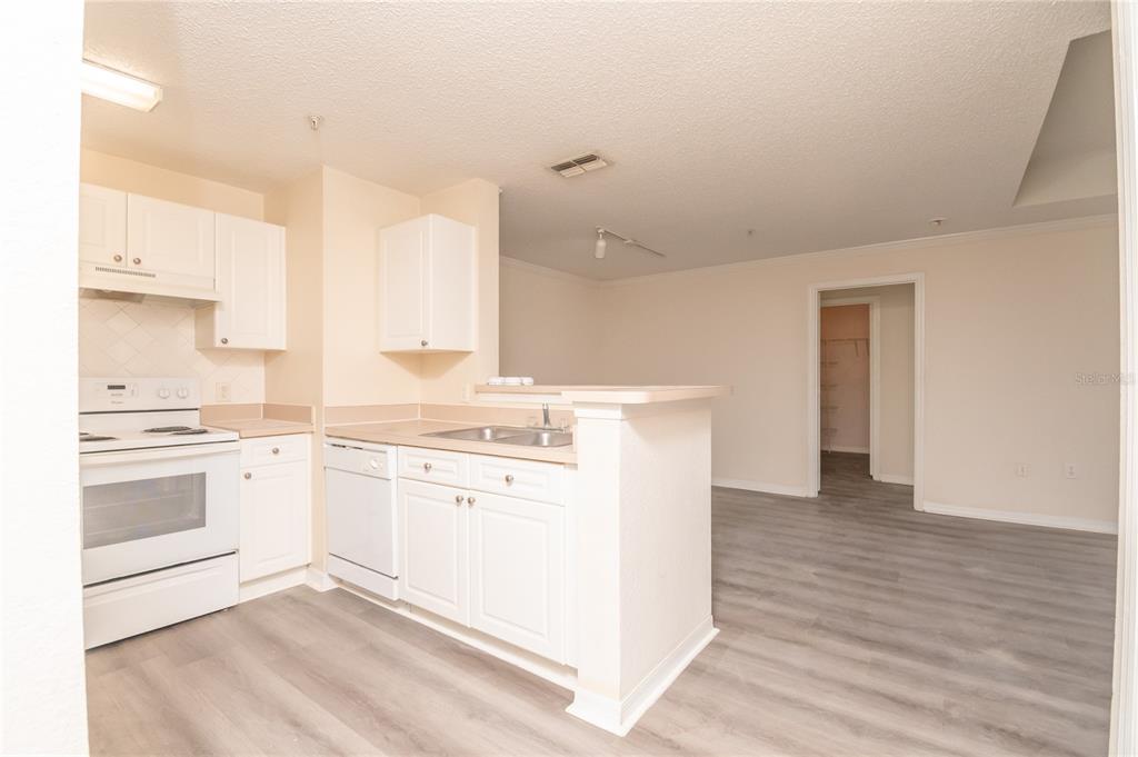 A kitchen with white cabinets and appliances overlooks an open living area with gray flooring — 18001 RICHMOND PLACE DRIVE UNIT 834, TAMPA, FL