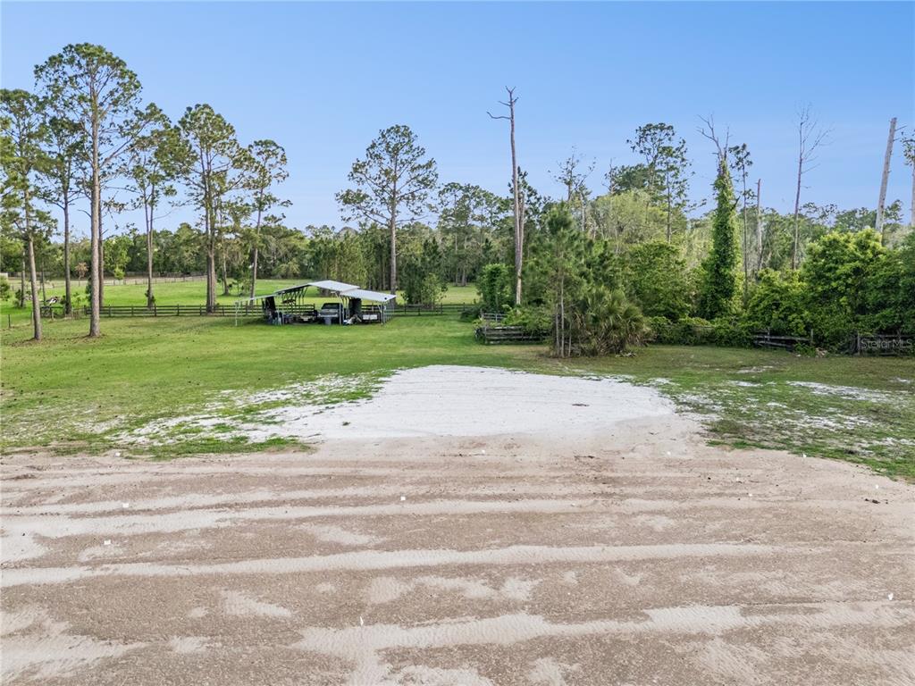 An open grassy lot features a metal carport structure and scattered trees under a blue sky — 110 WILD HORSE RUN, DELTONA, FL
