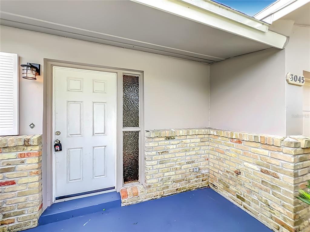A white front door with a side window sits on a blue porch with brick siding — 3045 AVON LANE, TITUSVILLE, FL