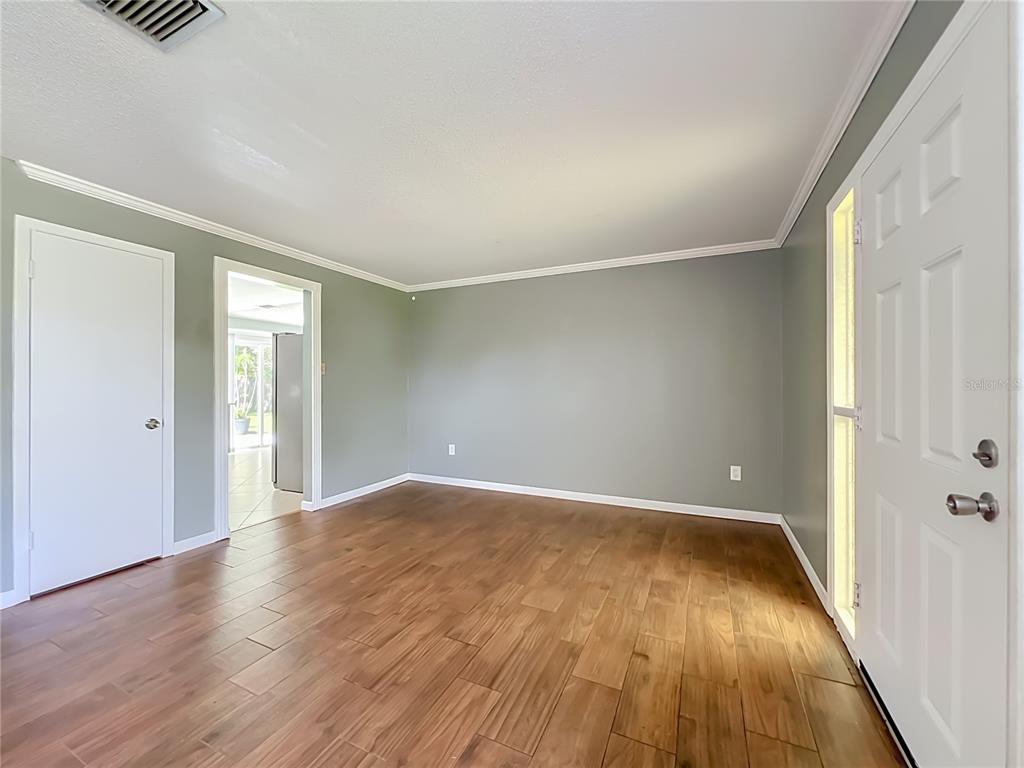An empty room features sage green walls, wood-look flooring, and a white front door — 3045 AVON LANE, TITUSVILLE, FL