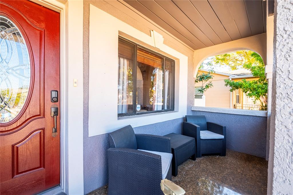 A covered front porch features a red door, two dark wicker chairs, and a small table — 2300 37TH AVENUE N, ST PETERSBURG, FL