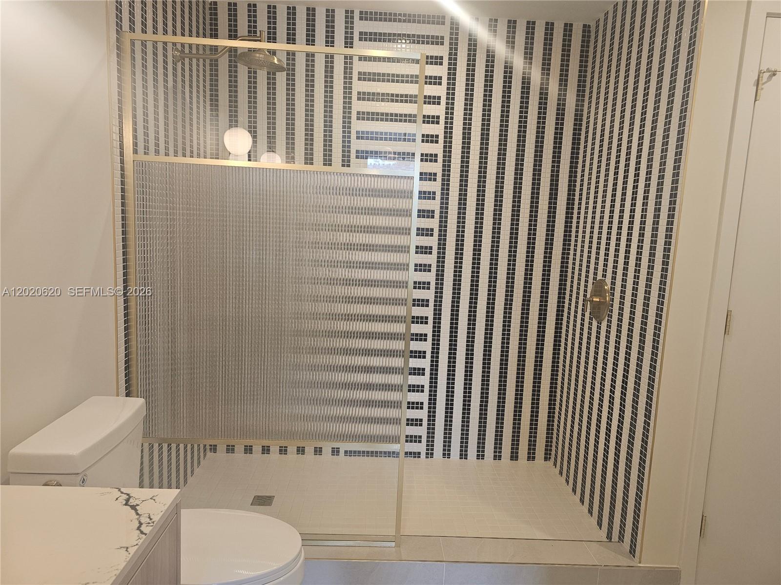 A bathroom features a walk-in shower with black and white striped tile and gold fixtures — 2700 NW 2nd Ave # 610, Miami FL 33127, MIAMI, FL