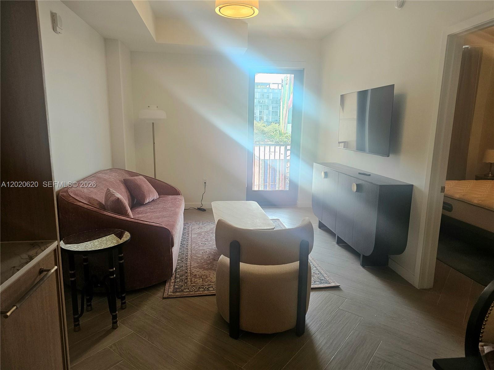 A living room features a mauve sofa, a beige accent chair, and a wall-mounted television — 2700 NW 2nd Ave # 610, Miami FL 33127, MIAMI, FL