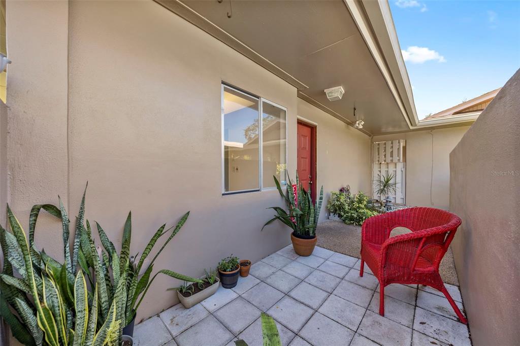 A paved patio features a red wicker chair, potted plants, and a red front door — 2484 LAURELWOOD DRIVE UNIT A, CLEARWATER, FL