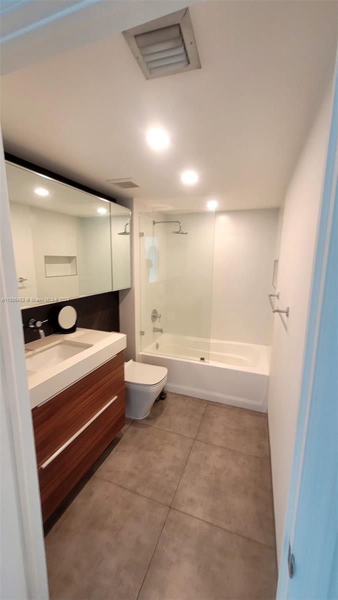 A modern bathroom features a wood vanity, a glass-enclosed shower-tub combo, and large floor tiles — 1155 Brickell Bay Dr # 2805, Miami FL 33131, MIAMI, FL