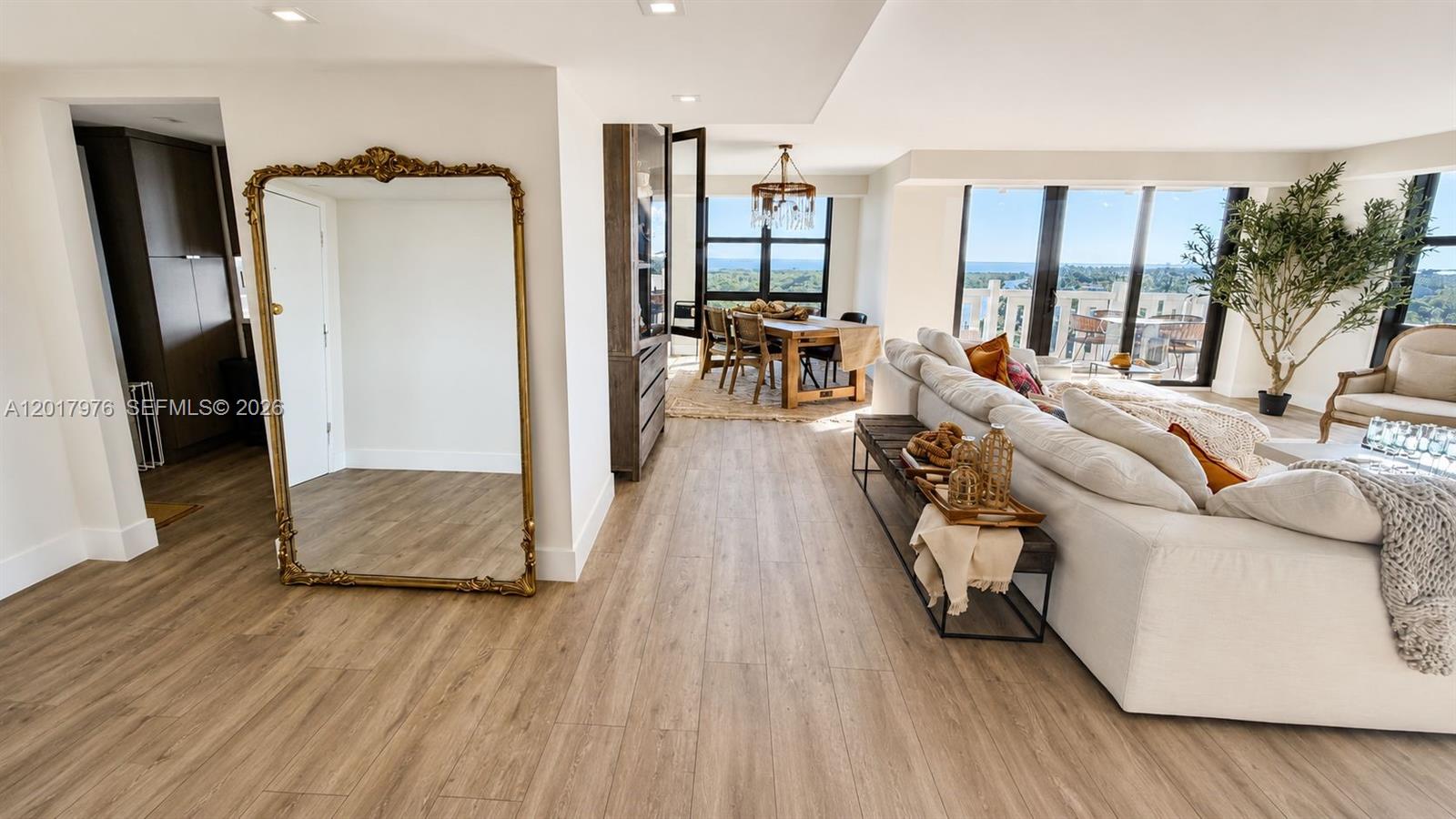 A bright living and dining area features light wood flooring, a large mirror, and floor-to-ceiling windows — 1121 Crandon Blvd # E708, Key Biscayne FL 33149, KEY BISCAYNE, FL
