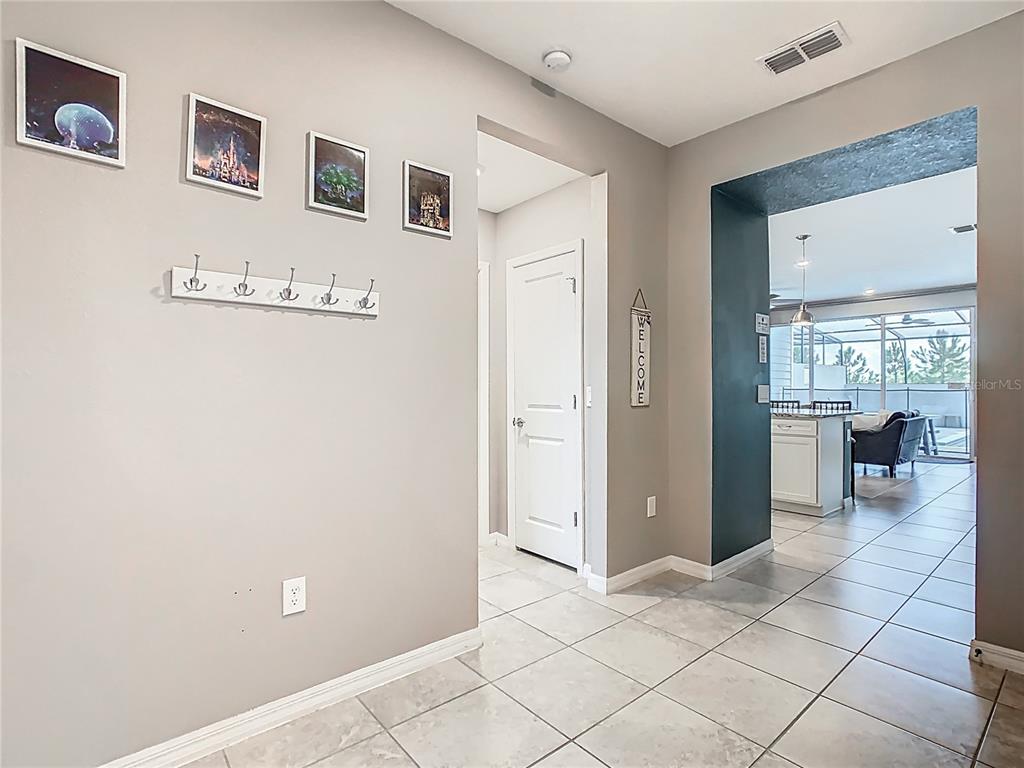 A tiled entryway features a coat rack, wall art, and a doorway leading to a kitchen — 967 PARADISE DRIVE, DAVENPORT, FL