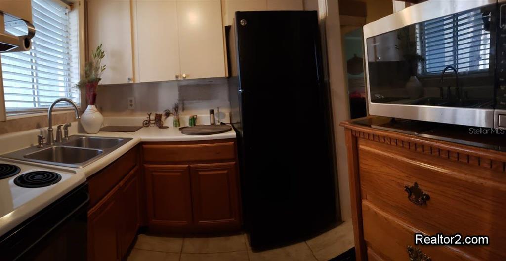 A kitchen features wooden cabinets, a black refrigerator, a double sink, and a microwave — 2047 CANAL DRIVE UNIT L6, BRADENTON, FL