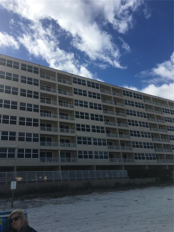 A multi-story beige residential building stands directly behind a sandy beach under a cloudy sky — 4453 S ATLANTIC AVENUE UNIT 208, PONCE INLET, FL