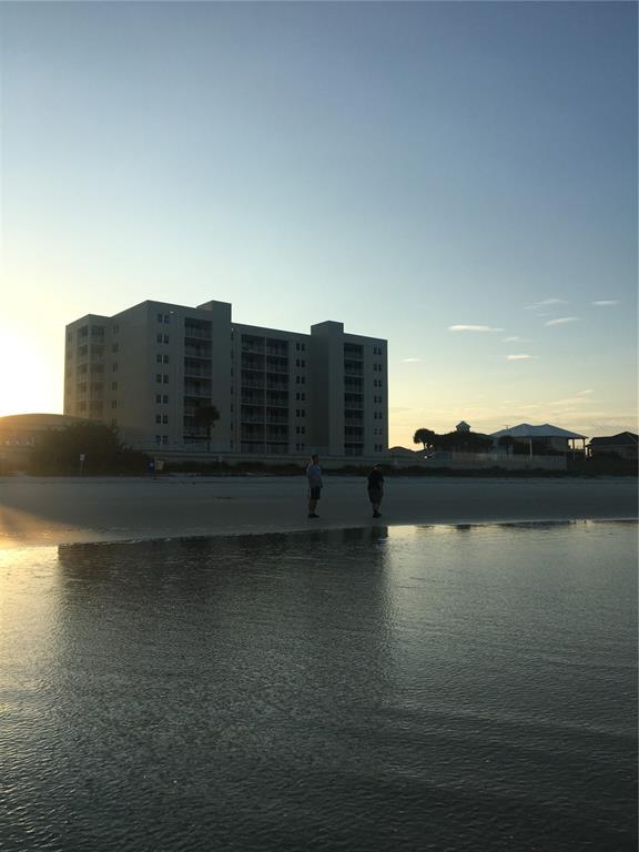A multi-story apartment building stands on a sandy beach at sunset with two people standing nearby — 4453 S ATLANTIC AVENUE UNIT 208, PONCE INLET, FL