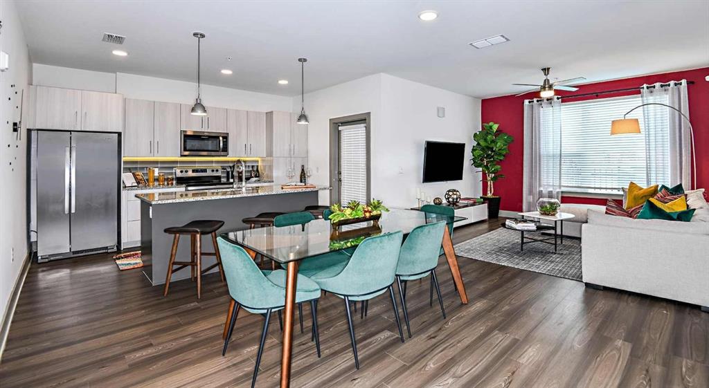 An open-concept kitchen, dining area, and living room featuring wood flooring and a red wall — 1040 JAMISON LOOP UNIT Revive, KISSIMMEE, FL