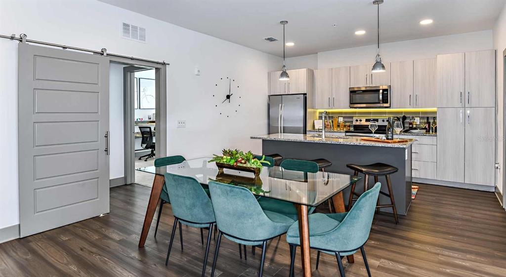 A modern kitchen with a dining area featuring a glass table and teal chairs — 1040 JAMISON LOOP UNIT Revive, KISSIMMEE, FL