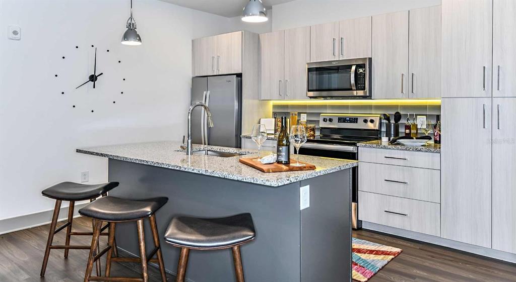 A modern kitchen features a gray island with bar stools, granite countertops, and light cabinetry — 1040 JAMISON LOOP UNIT Revive, KISSIMMEE, FL