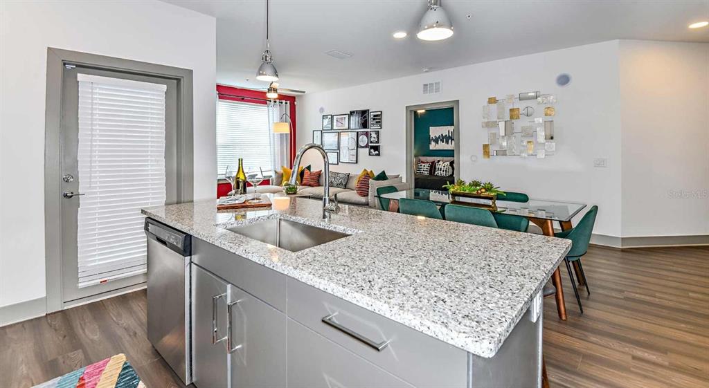 A kitchen island with a granite countertop and stainless steel sink overlooks a living area — 1040 JAMISON LOOP UNIT Revive, KISSIMMEE, FL