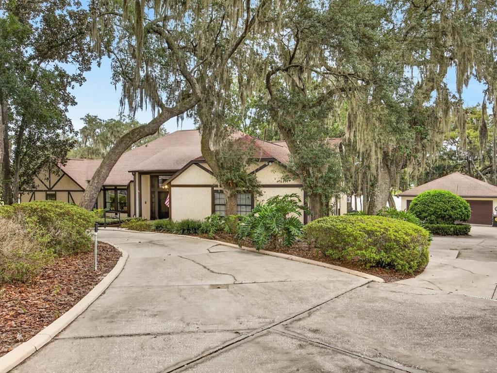 A stucco house with a brown roof and a curved driveway sits under large trees — 671 QUIETWATER COVE, ALTAMONTE SPRINGS, FL