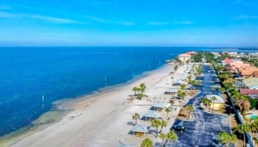 An aerial view of a sandy beach with palm trees, picnic shelters, and nearby buildings — 5245 AMULET DRIVE UNIT 102, NEW PORT RICHEY, FL