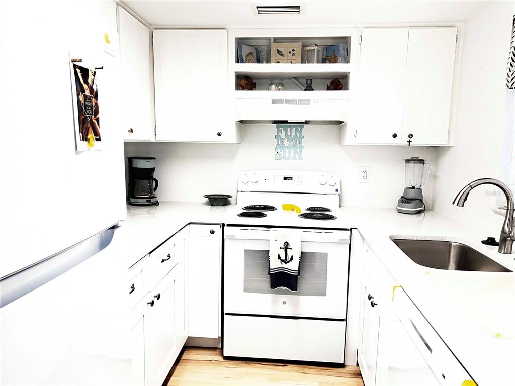 A white kitchen features white cabinets, a white stove, and a stainless steel sink — 5245 AMULET DRIVE UNIT 102, NEW PORT RICHEY, FL