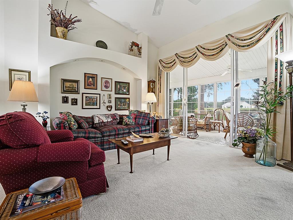 A living room features a plaid sofa, a red armchair, and sliding glass doors to a patio — 25069 RIVERWALK DRIVE, LEESBURG, FL