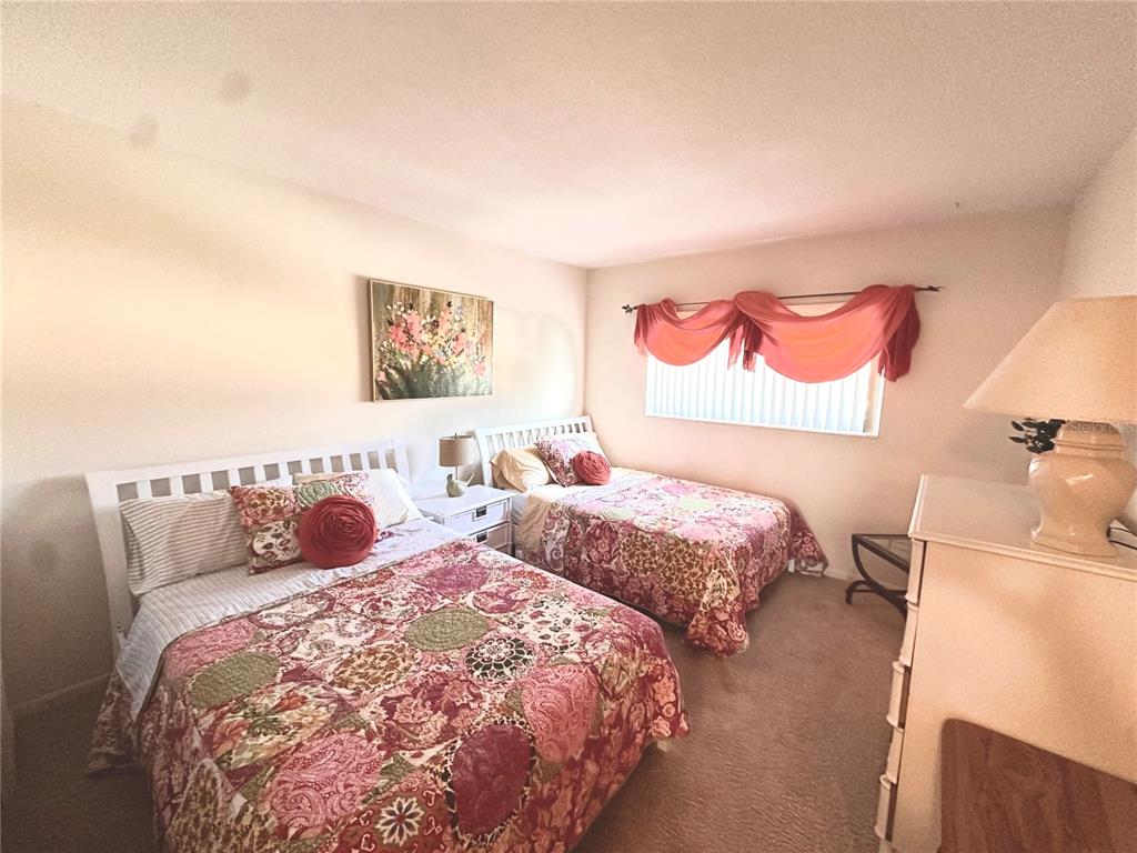 A bedroom features two beds with floral quilts, a white headboard, and a window with drapes — 1001 NE 8TH AVENUE UNIT 209, DELRAY BEACH, FL