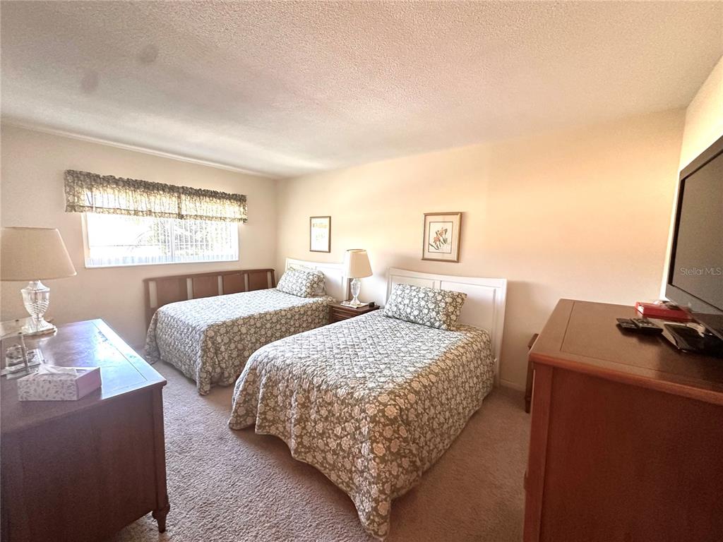 A bedroom features two twin beds with floral bedding, a dresser, and a television — 1001 NE 8TH AVENUE UNIT 209, DELRAY BEACH, FL