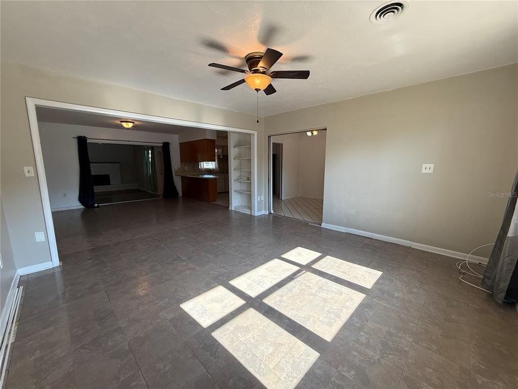 An empty living room features dark wood-look flooring, beige walls, and a ceiling fan — 915 14TH STREET E, BRADENTON, FL