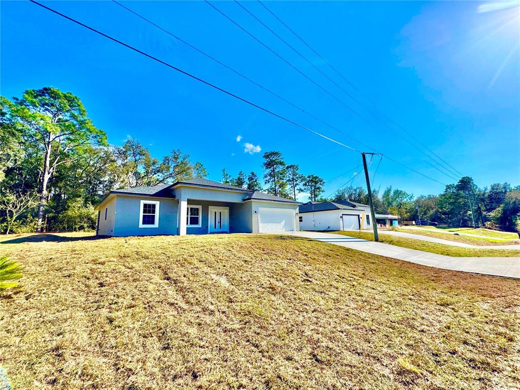 A modern, single-story gray house with a white garage and a sloped, grassy front yard — 10385 N CITRUS SPRINGS BOULEVARD, CITRUS SPRINGS, FL