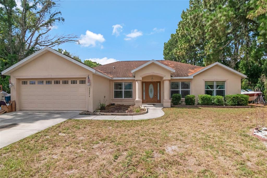 A single-story beige house features a two-car garage, a covered entryway, and a front lawn — 12276 VILLA ROAD, SPRING HILL, FL