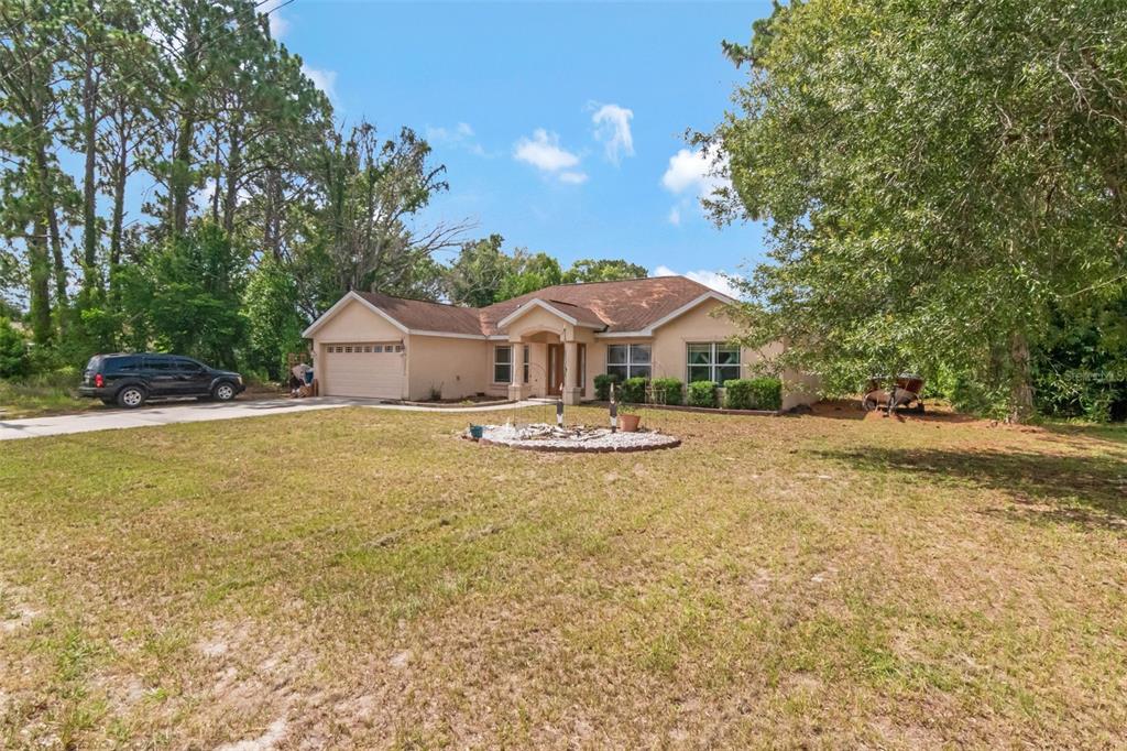 A single-story tan house with a two-car garage sits on a large, grassy lot — 12276 VILLA ROAD, SPRING HILL, FL