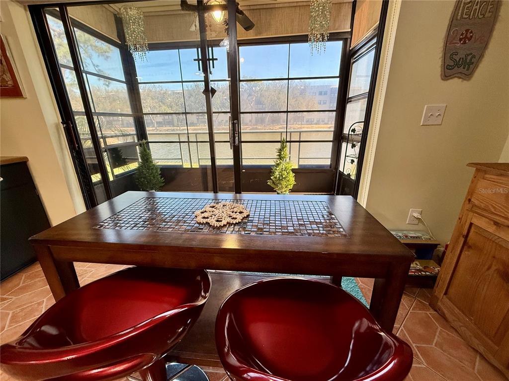 A dining area features a tiled-top table, red chairs, and a sliding door overlooking water — 6070 80TH STREET N UNIT 105, ST PETERSBURG, FL