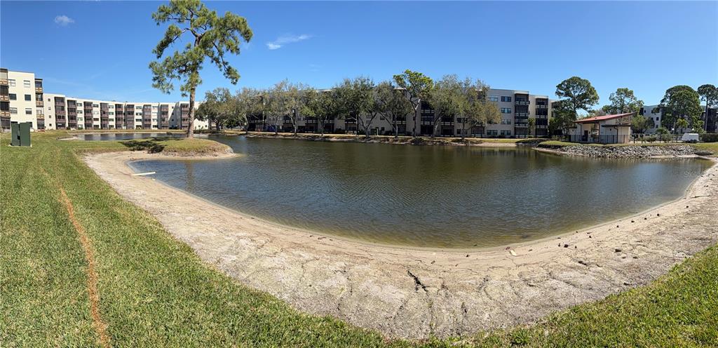 A panoramic view of a pond surrounded by apartment buildings and a grassy lawn — 6070 80TH STREET N UNIT 105, ST PETERSBURG, FL