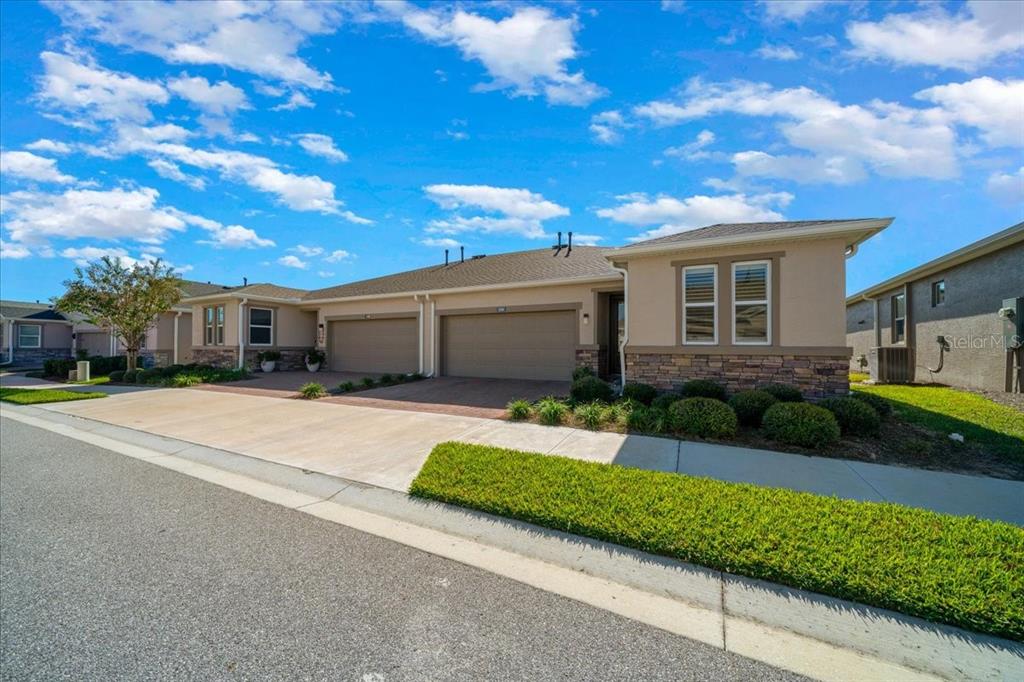 A tan, single-story duplex with two garage doors and stone accents under a blue sky — 5360 NW 34TH STREET, OCALA, FL