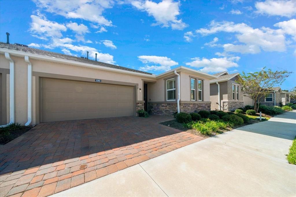 A beige house with a stone facade, a two-car garage, and a brick paver driveway — 5360 NW 34TH STREET, OCALA, FL