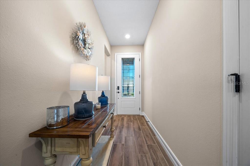 A hallway features wood-look tile flooring, a console table with lamps, and a glass-paneled front door — 5360 NW 34TH STREET, OCALA, FL