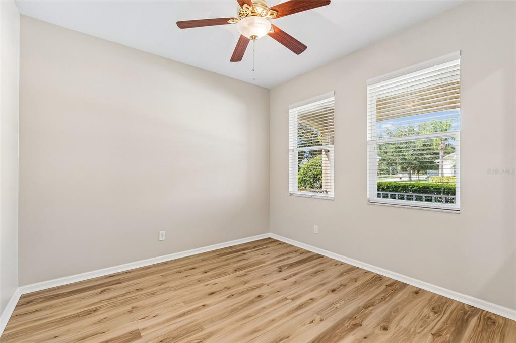 An empty room with light-colored walls, wood-look flooring, two windows, and a ceiling fan — 19110 SUNSET BAY DRIVE, LAND O LAKES, FL