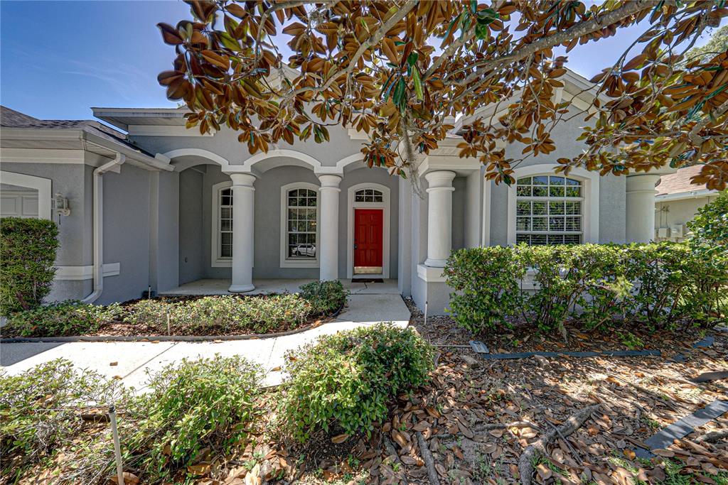 A gray house exterior features a red front door, white columns, and a covered porch — 1603 GRAND HERITAGE BOULEVARD, VALRICO, FL