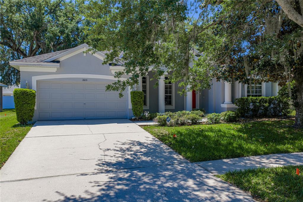 A gray house exterior features a red front door, arched columns, and a landscaped yard — 1603 GRAND HERITAGE BOULEVARD, VALRICO, FL