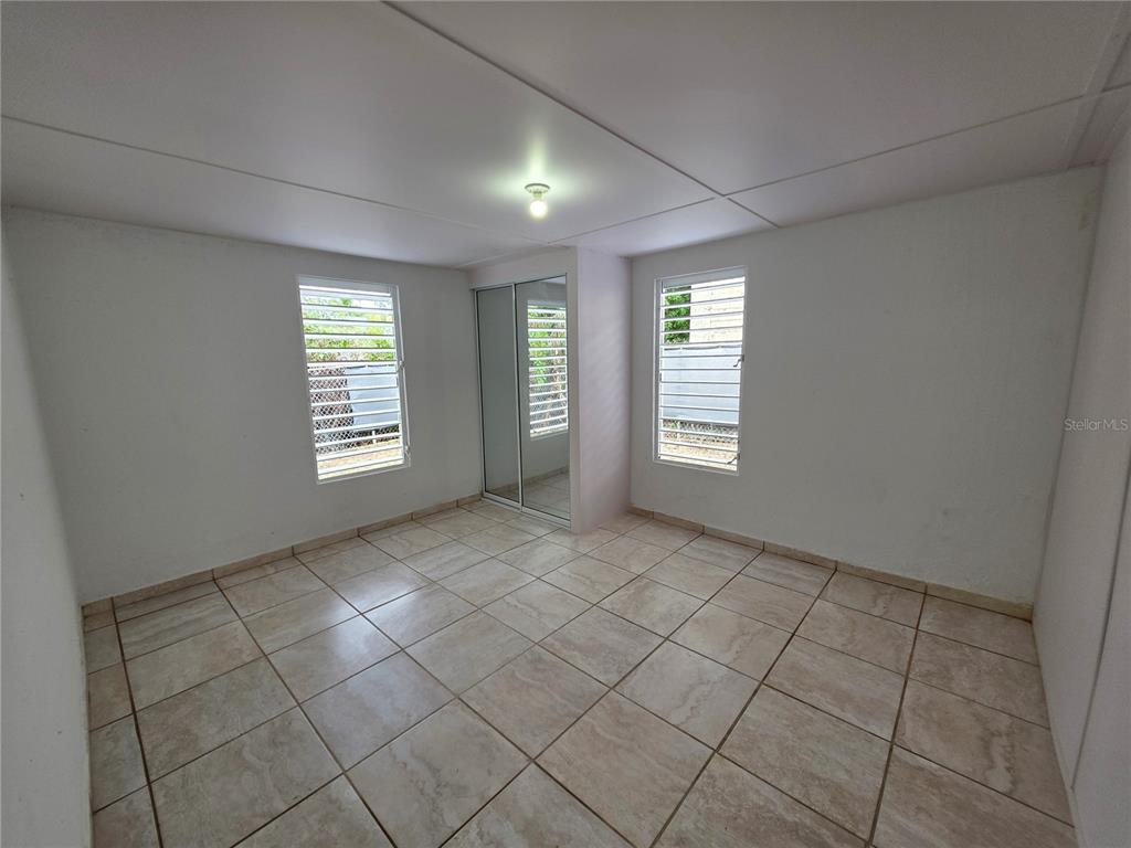 An empty bedroom features white walls, tiled flooring, two louvered windows, and a mirrored closet — 657 ST BO. ARRENALEJOS #4, ARECIBO, PR