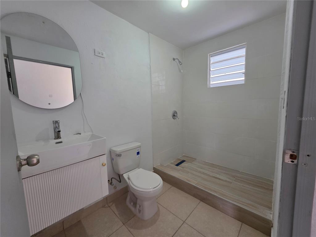 A bathroom features a white vanity, a round mirror, a toilet, and a tiled walk-in shower — 657 ST BO. ARRENALEJOS #4, ARECIBO, PR