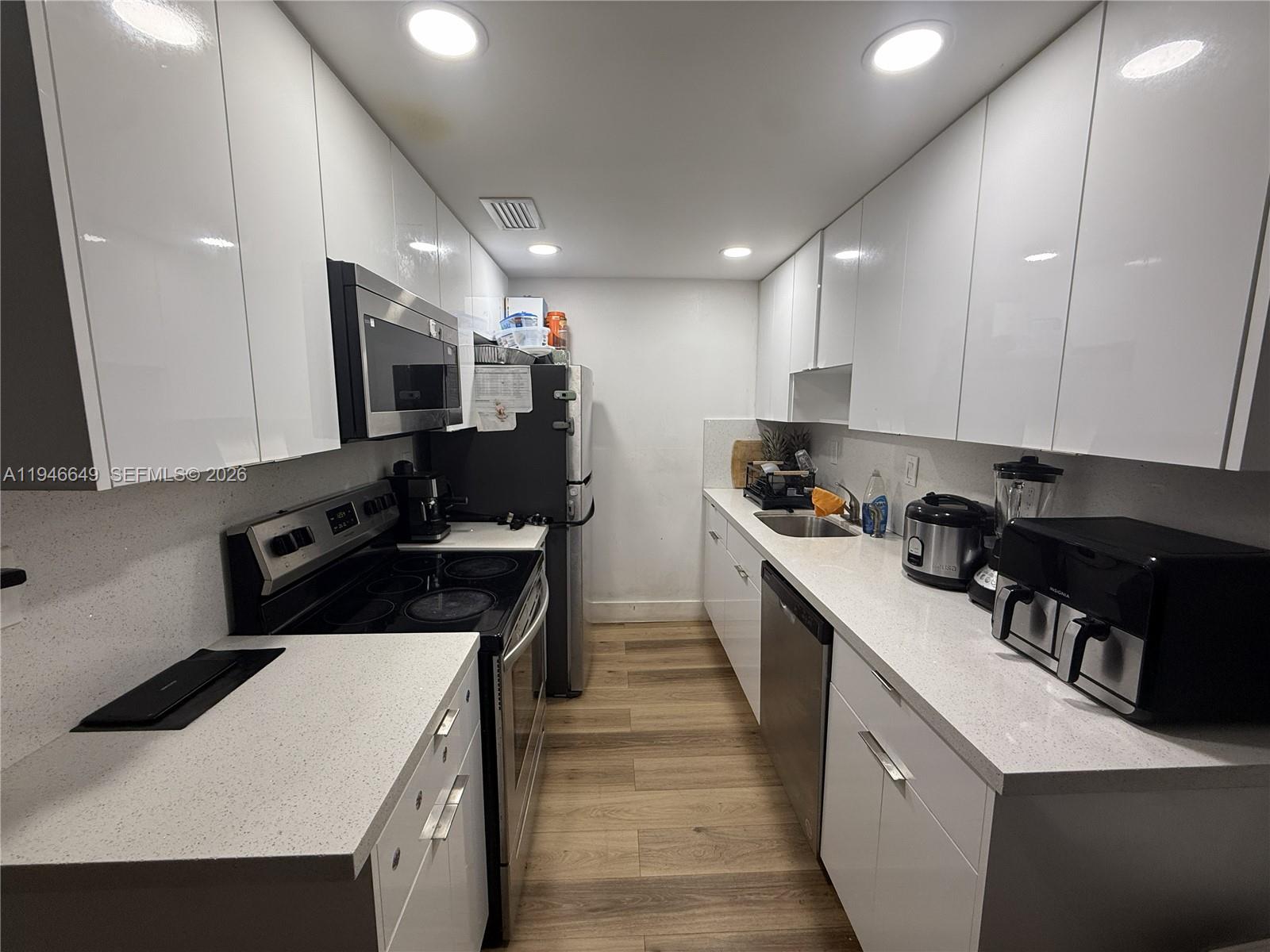 A galley kitchen features white flat-panel cabinets, stainless steel appliances, and light-colored quartz countertops — 10822 N Kendall Dr # S23, Miami FL 33176, MIAMI, FL