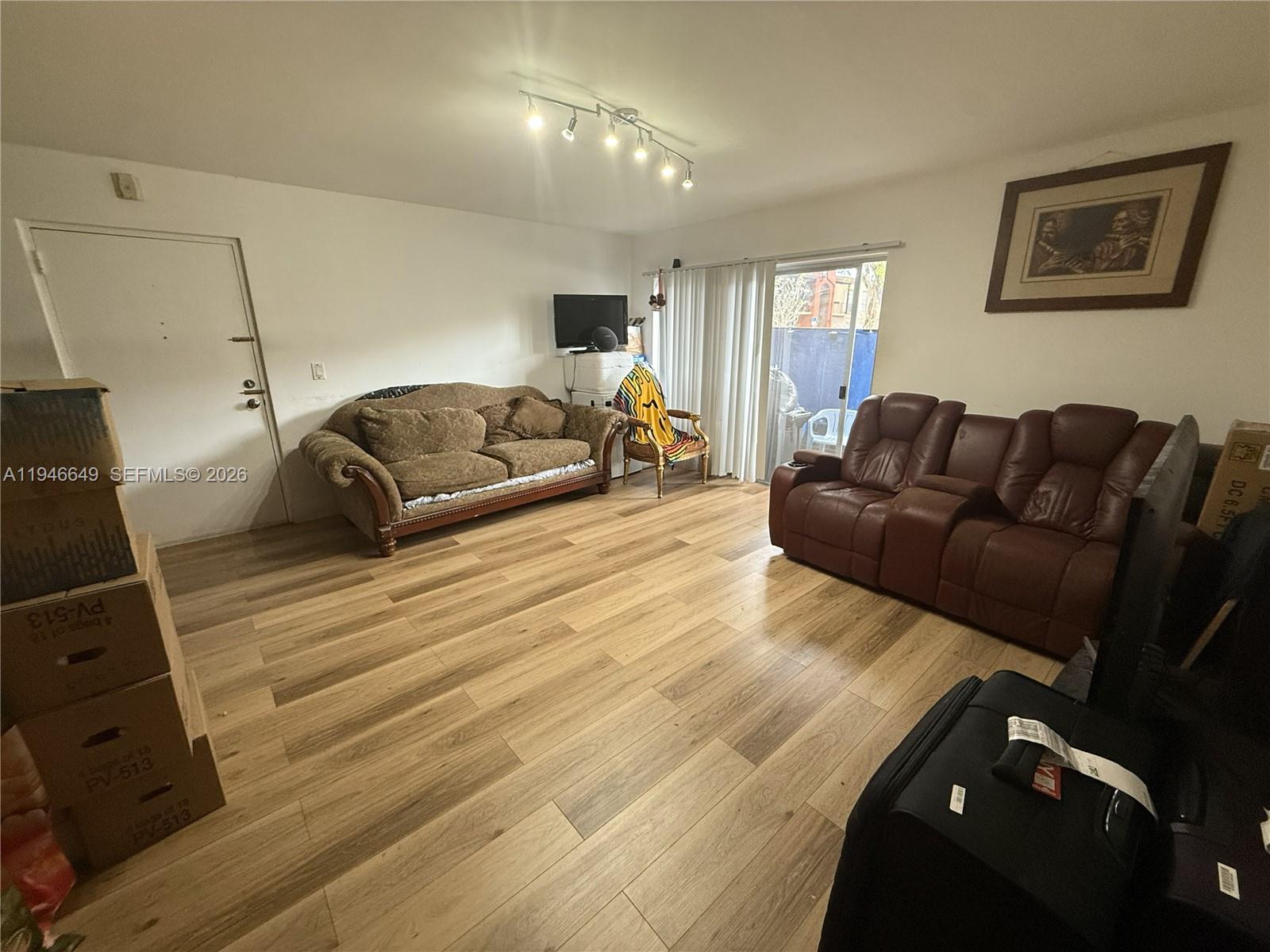 A living room features wood-look flooring, two sofas, a sliding glass door, and overhead lighting — 10822 N Kendall Dr # S23, Miami FL 33176, MIAMI, FL