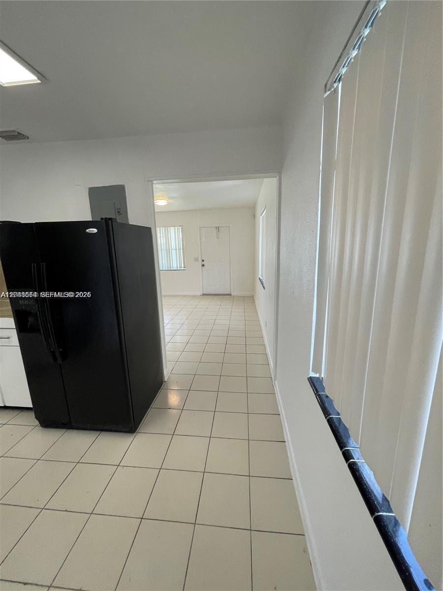 A kitchen with white tile floors and a black refrigerator leads into an adjacent room — 2435 Plunkett St # 1, Hollywood FL 33020, HOLLYWOOD, FL