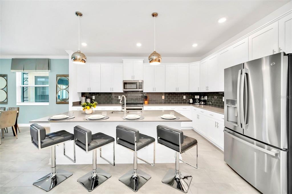 A modern kitchen features white cabinetry, a large island with four barstools, and stainless appliances — 2661 PETITION LANE, KISSIMMEE, FL