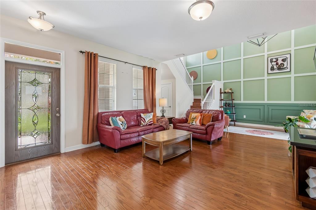 A living room features hardwood floors, red leather sofas, and a green paneled accent wall — 13344 GRAHAM YARDEN, RIVERVIEW, FL