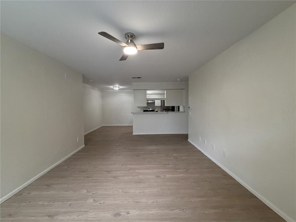 An open-concept living area features light wood-look flooring, a ceiling fan, and a kitchen pass-through — 36101 DEER CREEK DRIVE UNIT 103, ZEPHYRHILLS, FL