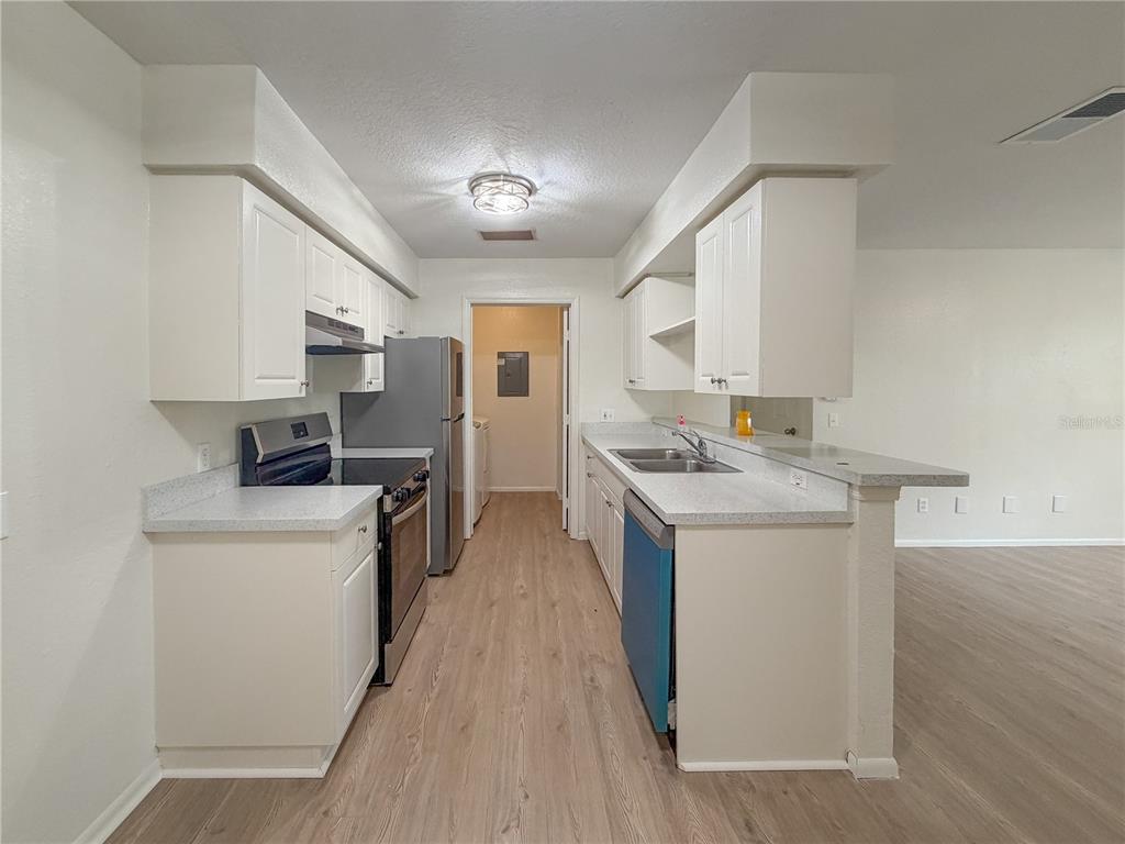 A galley-style kitchen features white cabinets, light countertops, stainless steel appliances, and wood-look flooring — 36101 DEER CREEK DRIVE UNIT 103, ZEPHYRHILLS, FL