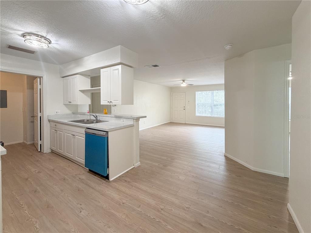 A kitchen with white cabinets and a blue dishwasher opens into a spacious living area — 36101 DEER CREEK DRIVE UNIT 103, ZEPHYRHILLS, FL