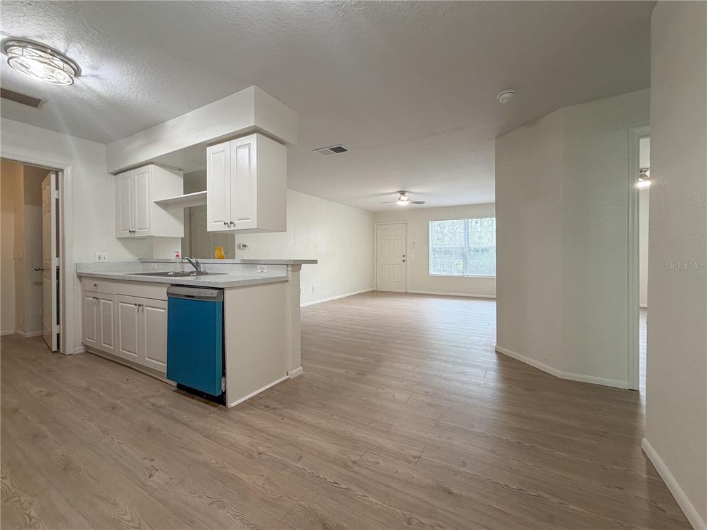 A kitchen with white cabinets and a blue dishwasher opens into a spacious living area — 36101 DEER CREEK DRIVE UNIT 103, ZEPHYRHILLS, FL