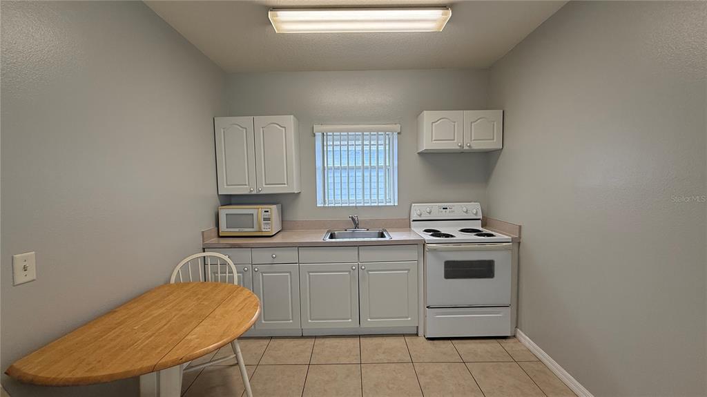 A small kitchen features white cabinets, a white stove, a sink, and a wooden table — 627 ORCHID DRIVE, DAVENPORT, FL